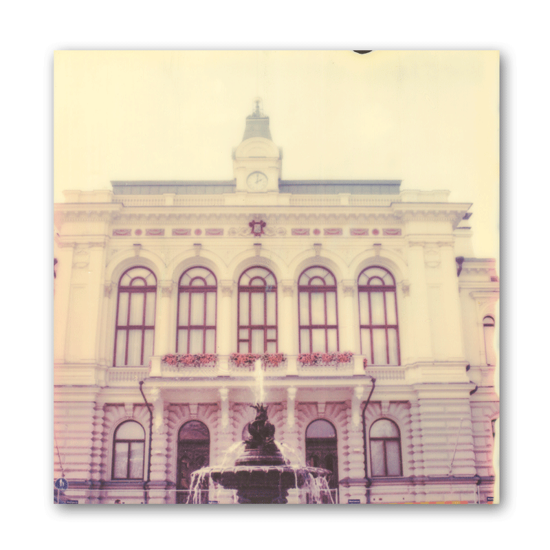 Polroid eines weißen Rathauses mit Springbrunnen.