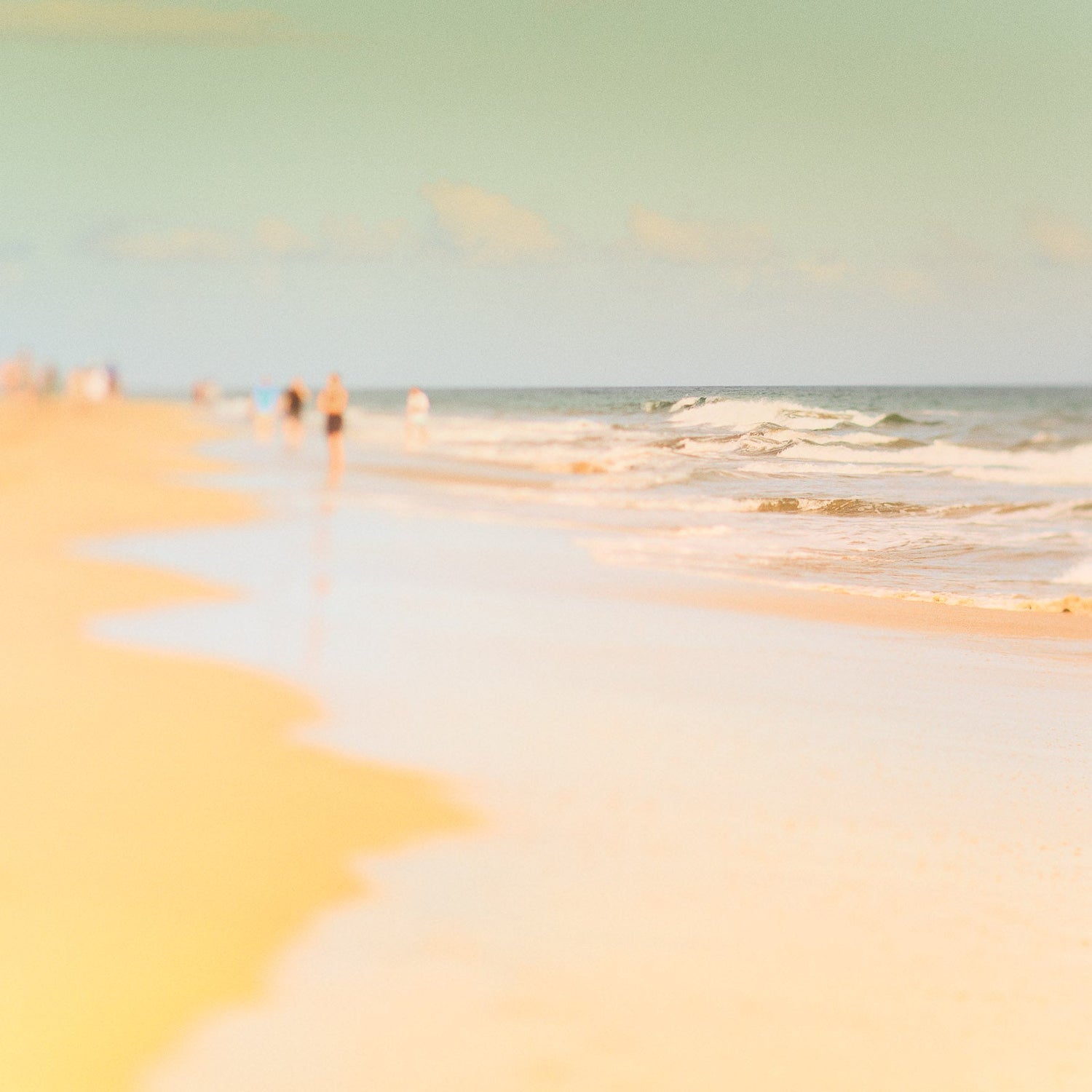 Ein quadratisches Bild von Wellen, die an einen Strand fliessen und unscharf Menschen im Hintergrund